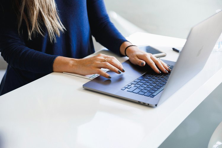 Immobilienberatung digital vorbereiten Person arbeitet an einem Laptop auf einem hellen Schreibtisch, daneben liegen Smartphone und Notizzettel.