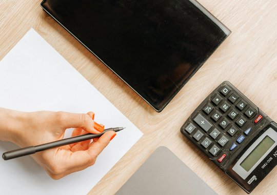 Person hält Stift neben dran liegt ein Taschenrechner und Block 