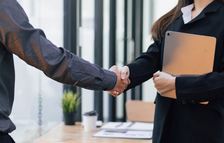 Professioneller Geschäftsabschluss im Büro Geschäftliches Händeschütteln zwischen zwei Personen im Büro, eine davon hält ein Tablet in der Armbeuge.