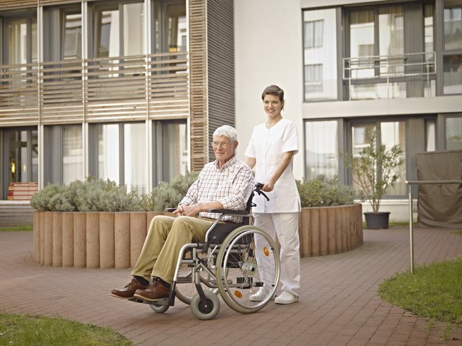 Altenpflegerin mit Rollstuhl vor einer Immobilie 