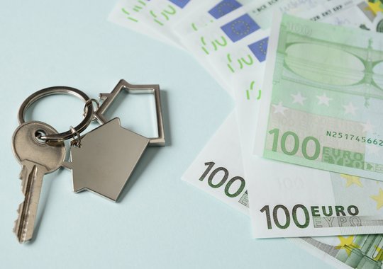 Schlüssel mit Haus-Anhänger neben mehreren 100-Euro-Scheinen – Symbol für Immobilienkauf und Finanzierung.